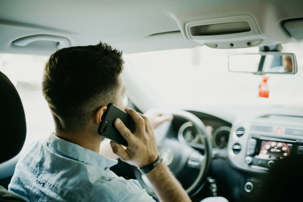 image of an employee talking on cell phone behind the wheel, one of the four types of distracted driving